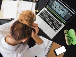 brunette holding her head in her heands in front of a laptop