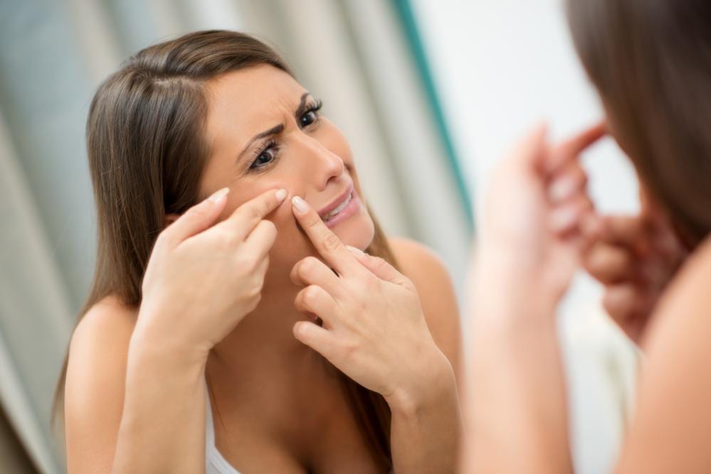 brunette popping acne in mirror