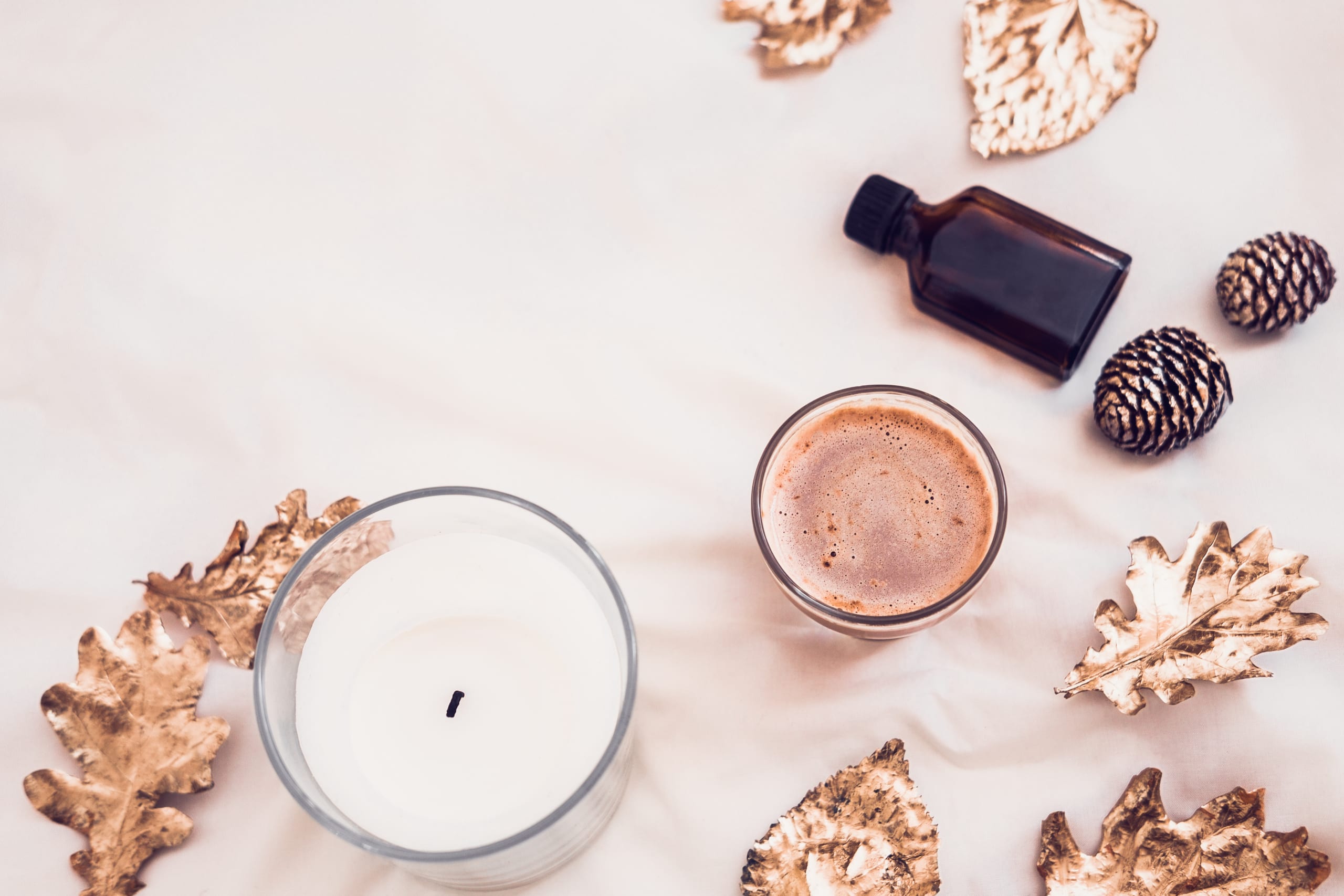 white candle next to coffee & autumn leaves on a cream background